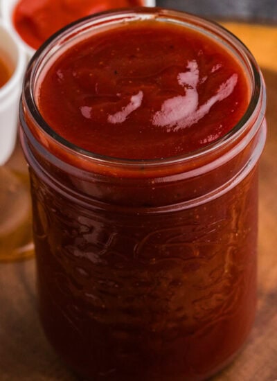 Jar of homemade Honey Sriracha BBQ Sauce with honey and Sriracha in the background.