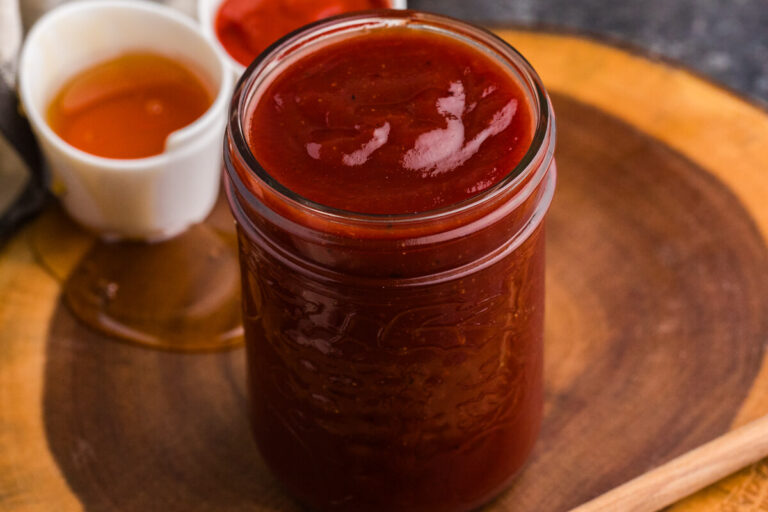 Jar of homemade Honey Sriracha BBQ Sauce with honey and Sriracha in the background.