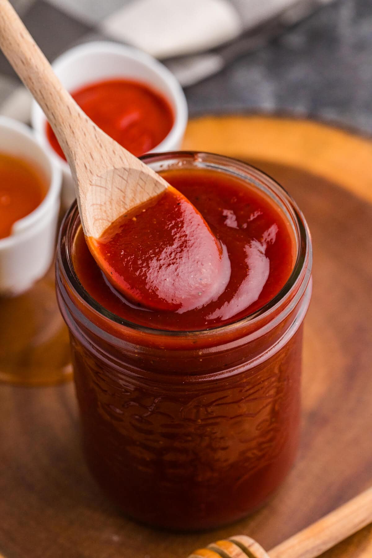 Wooden spoon coated with glossy Honey Sriracha BBQ Sauce over a jar of homemade sauce.
