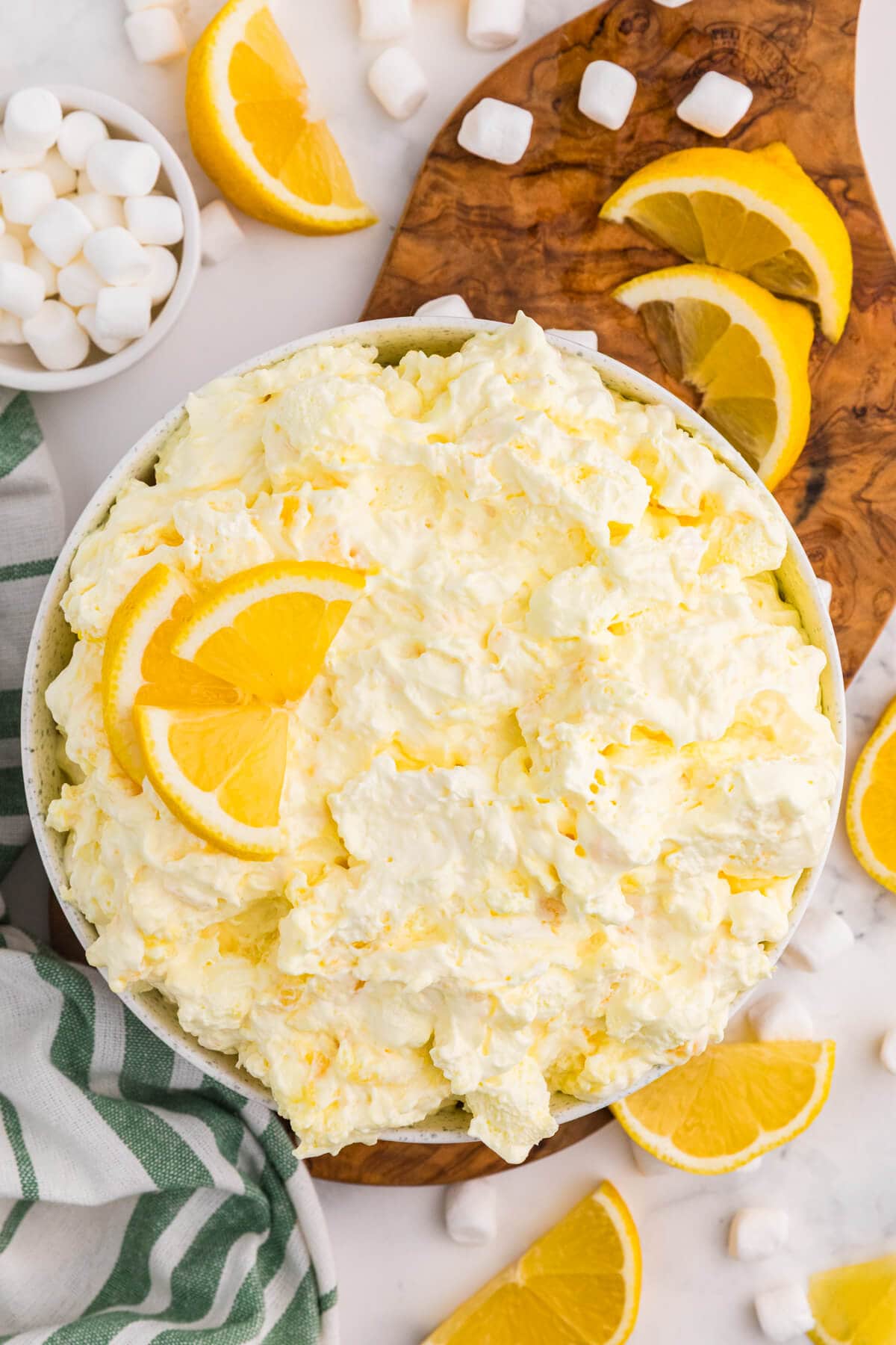 Lemon Fluff dessert salad topped with lemon slices, surrounded by mini marshmallows and fresh lemon wedges.