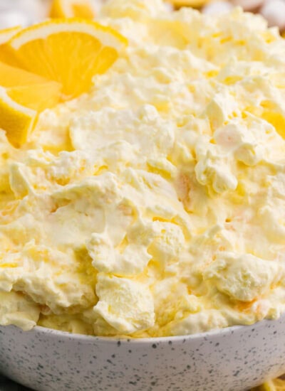 Bowl of creamy Lemon Fluff dessert salad with pineapple and marshmallows, garnished with fresh lemon slices.