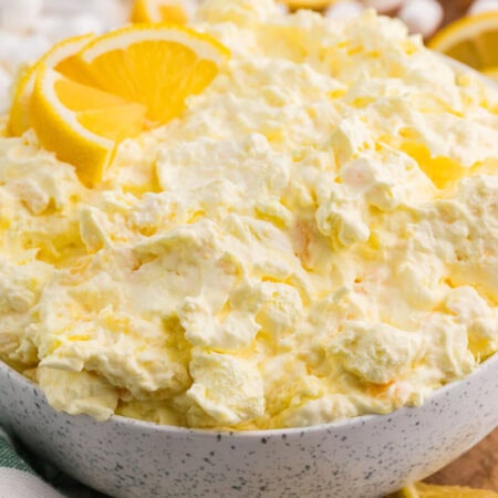 Bowl of creamy Lemon Fluff dessert salad with pineapple and marshmallows, garnished with fresh lemon slices.