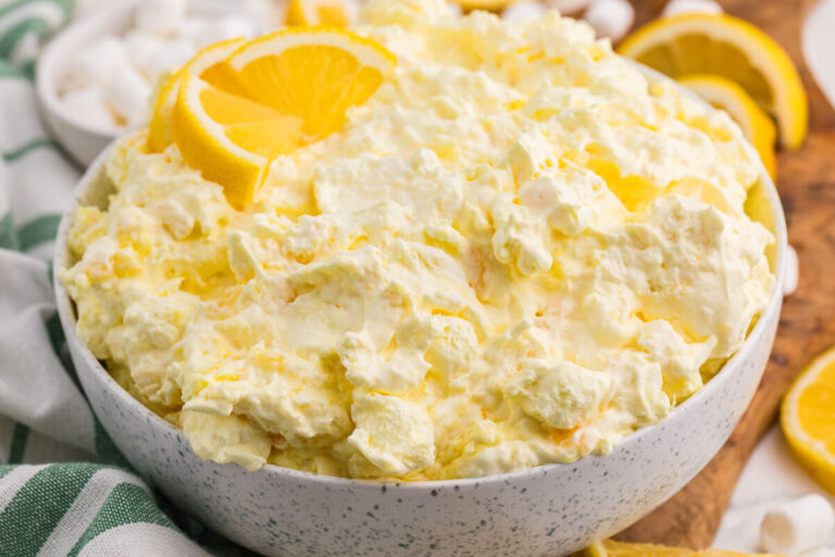 Bowl of creamy Lemon Fluff dessert salad with pineapple and marshmallows, garnished with fresh lemon slices.