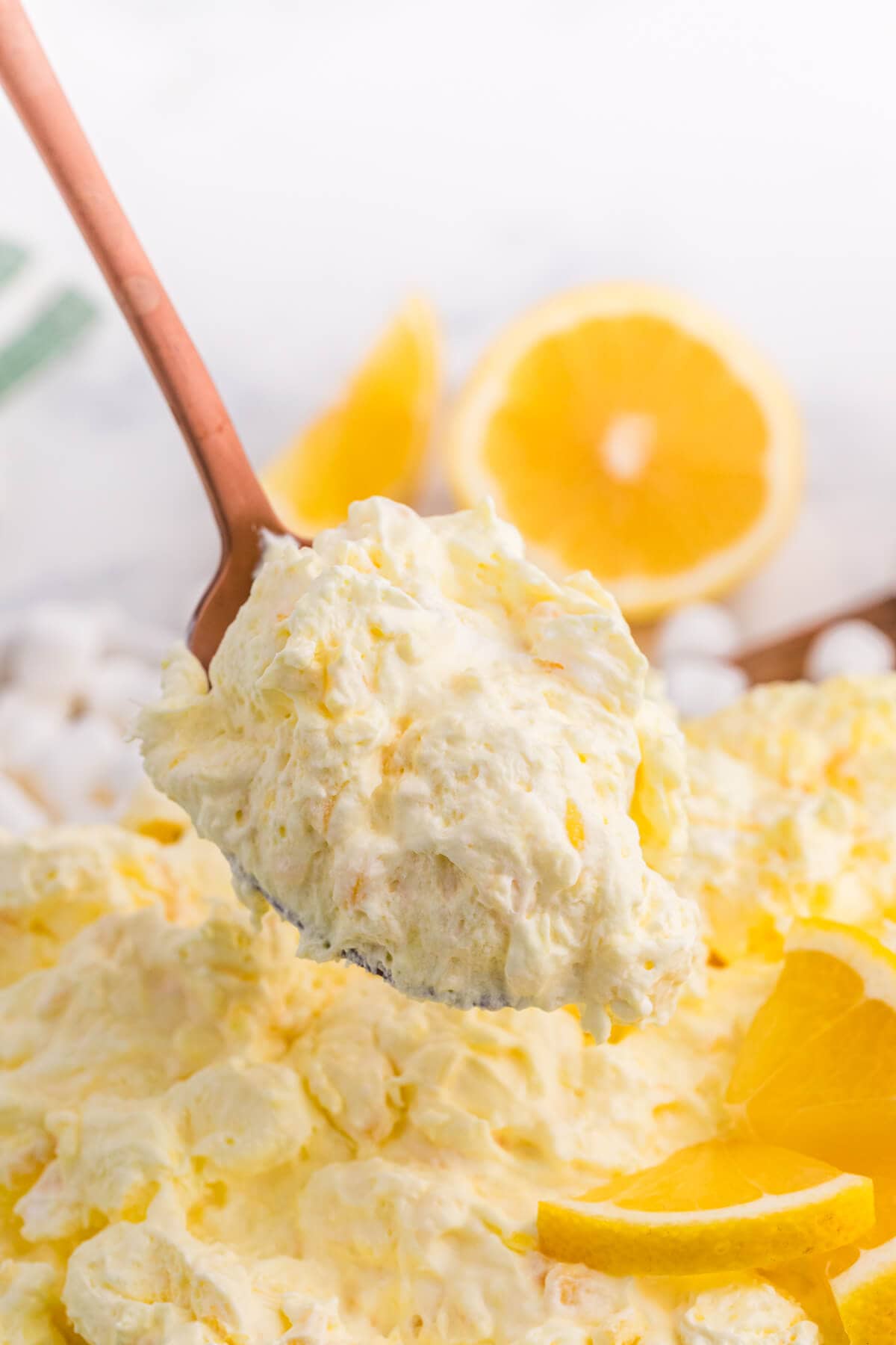 Spoonful of creamy Lemon Fluff dessert salad showing its thick, fluffy texture, with lemon slices in the background.