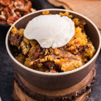 Bowl of Maple Syrup Dump Cake with pecans topped with a scoop of vanilla ice cream.