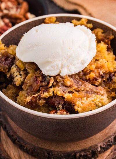 Bowl of Maple Syrup Dump Cake with pecans topped with a scoop of vanilla ice cream.