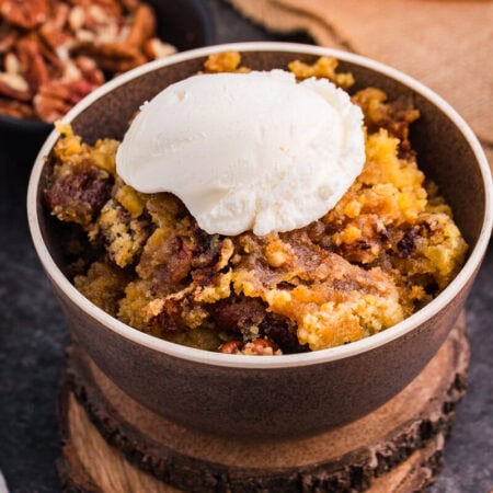 Bowl of Maple Syrup Dump Cake with pecans topped with a scoop of vanilla ice cream.