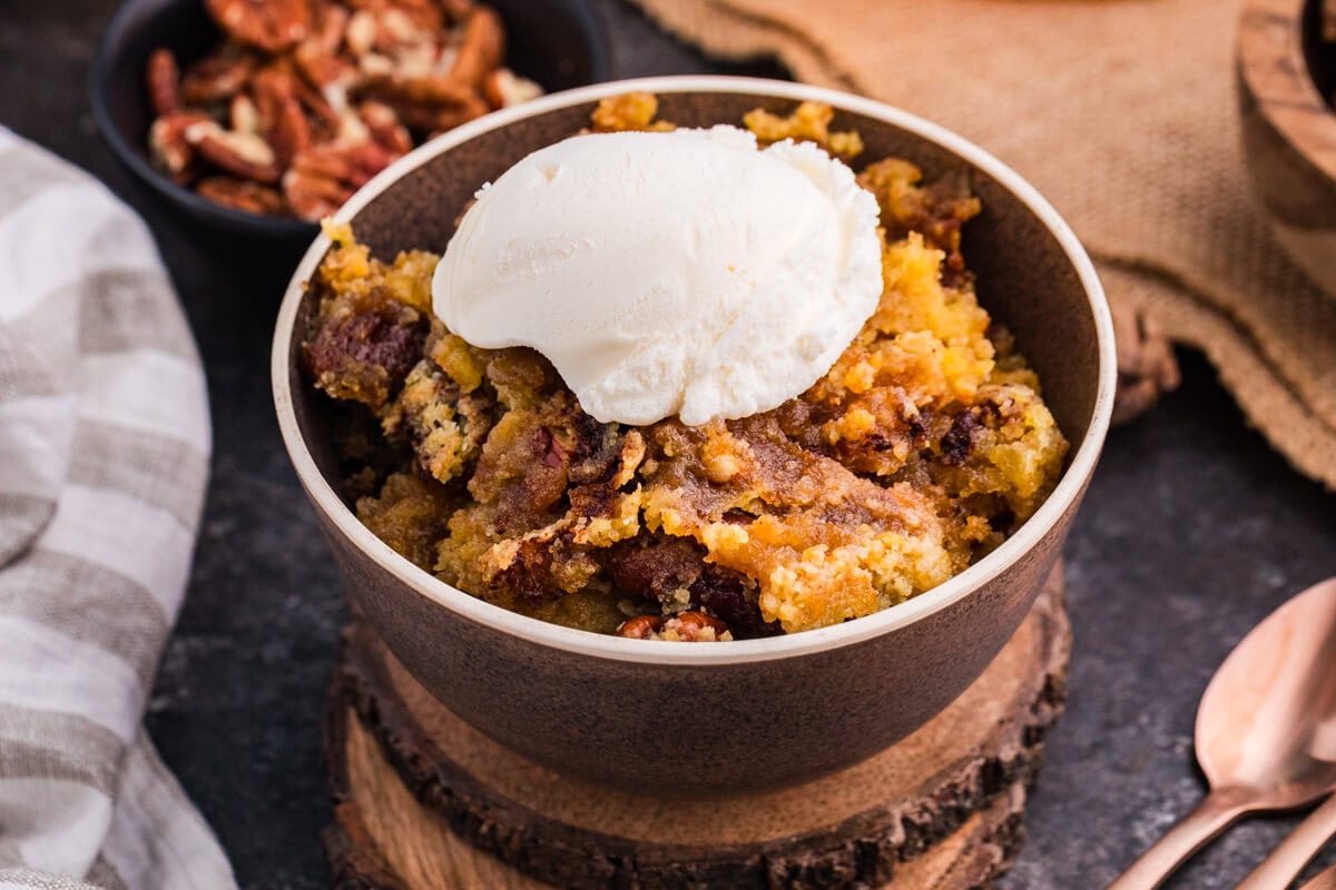 Bowl of Maple Syrup Dump Cake with pecans topped with a scoop of vanilla ice cream.