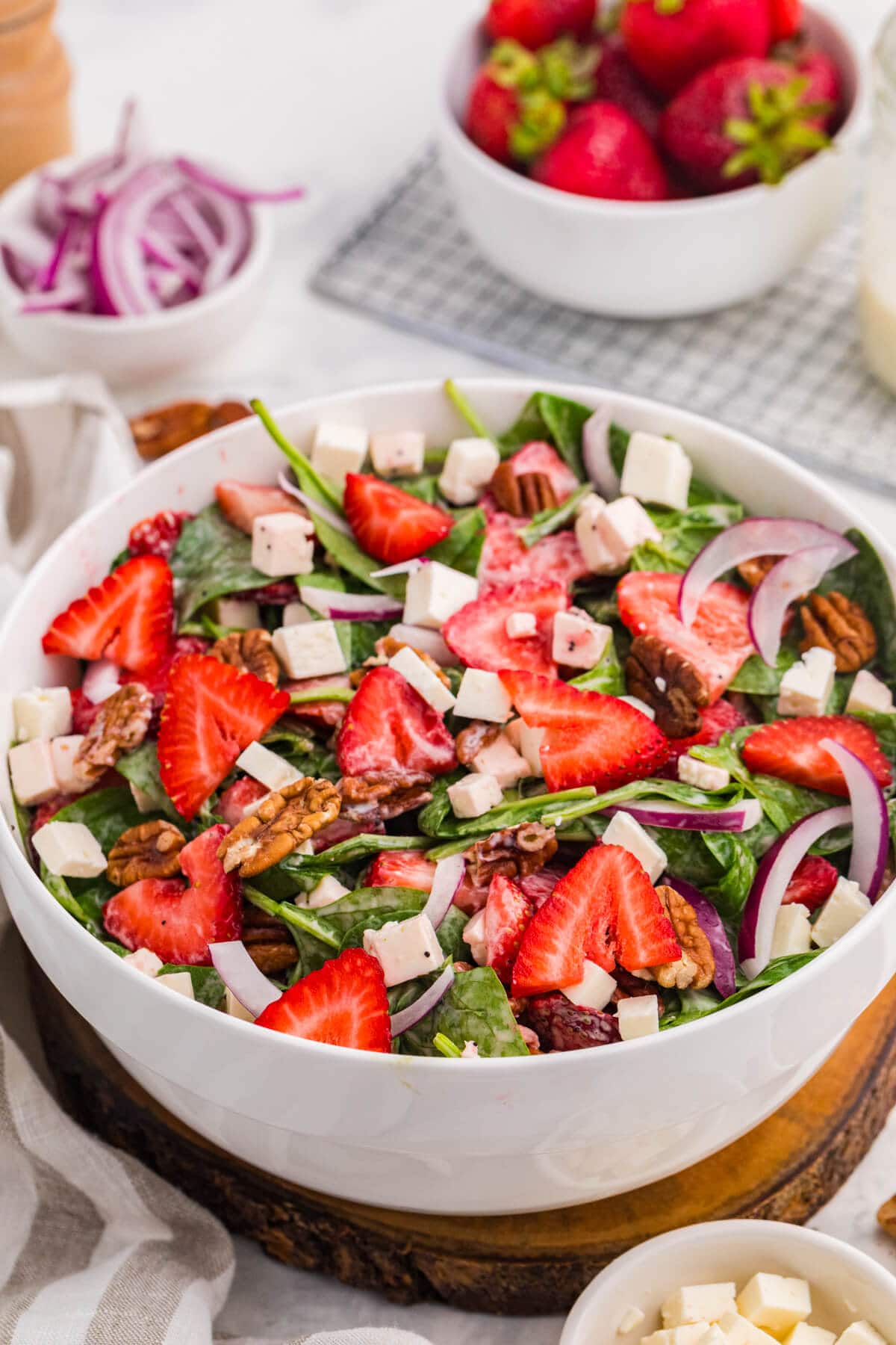 Strawberry spinach salad with sliced strawberries, feta cheese, toasted pecans, red onion, and creamy poppyseed dressing in a white bowl.