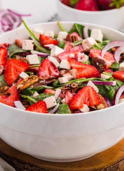 Strawberry spinach salad with fresh strawberries, feta cheese, toasted pecans, red onion, and creamy poppyseed dressing in a white serving bowl.
