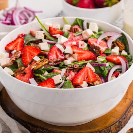 Strawberry spinach salad with fresh strawberries, feta cheese, toasted pecans, red onion, and creamy poppyseed dressing in a white serving bowl.