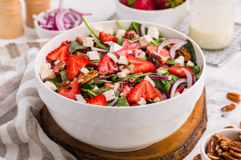 Strawberry spinach salad with fresh strawberries, feta cheese, toasted pecans, red onion, and creamy poppyseed dressing in a white serving bowl.