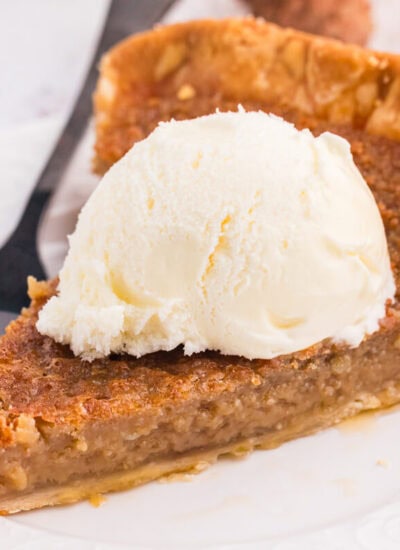 Slice of Maple Syrup Pie topped with a scoop of vanilla ice cream on a white plate.