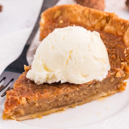 Slice of Maple Syrup Pie topped with a scoop of vanilla ice cream on a white plate.