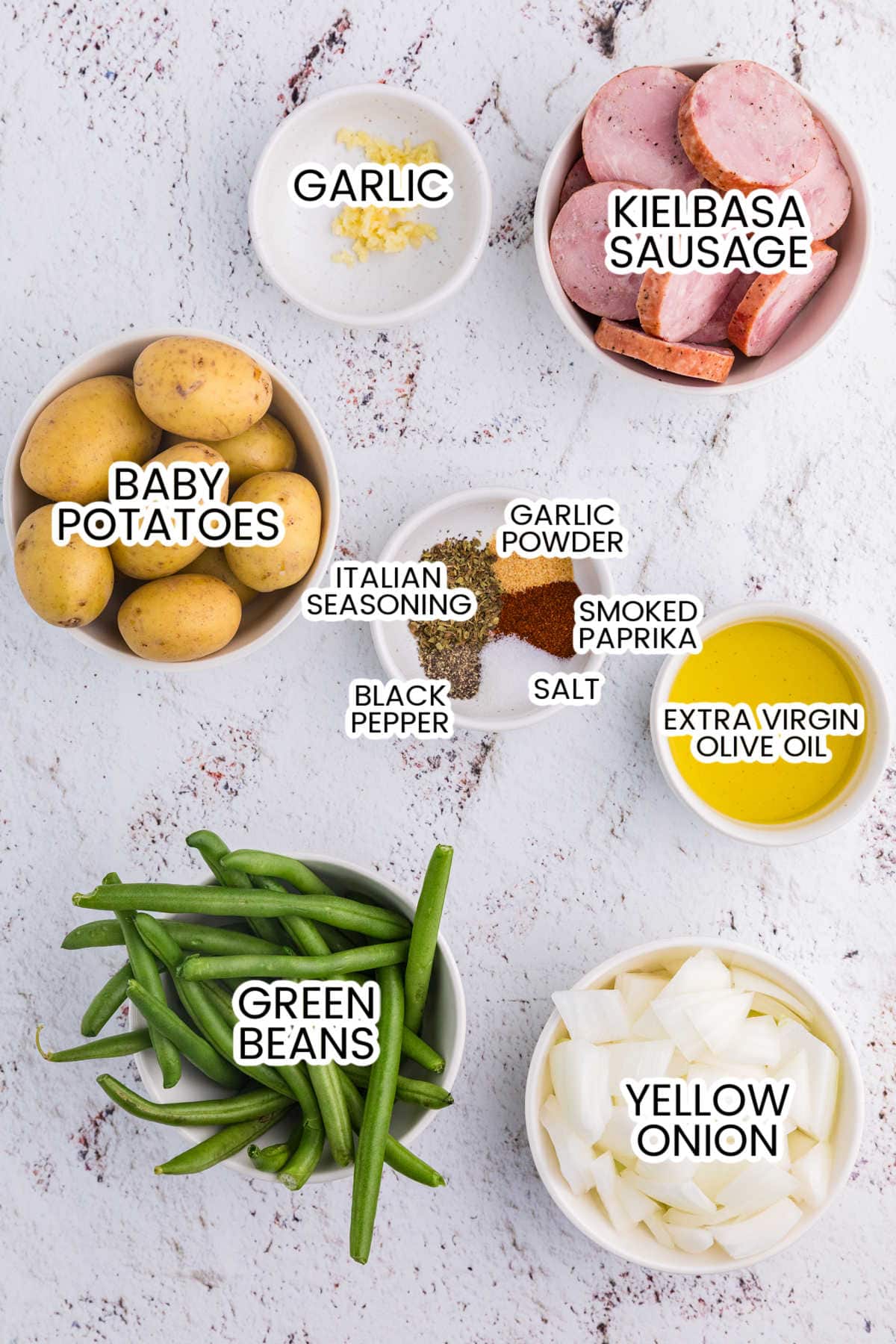 Ingredients for sheet pan sausage, potatoes and green beans, including kielbasa, baby potatoes, green beans, onion, garlic, olive oil, and seasonings.