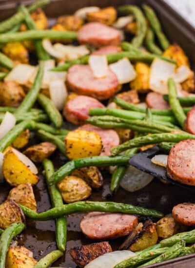 Sheet pan sausage, potatoes and green beans with browned kielbasa, roasted baby potatoes, green beans, and onion being served from the pan.