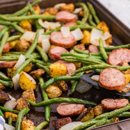 Sheet pan sausage, potatoes and green beans with browned kielbasa, roasted baby potatoes, green beans, and onion being served from the pan.