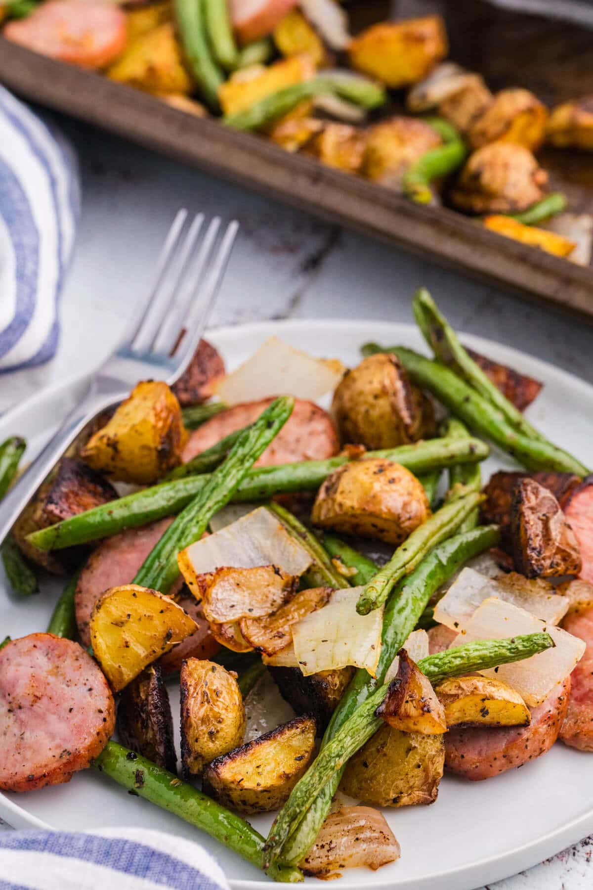 Plate of sheet pan sausage, potatoes and green beans with roasted kielbasa, baby potatoes, onion, and green beans.
