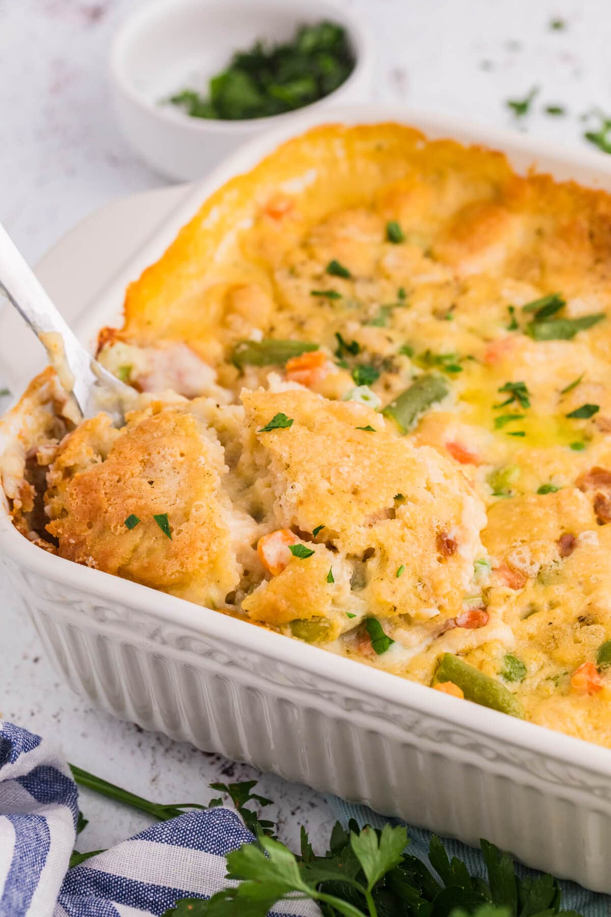 TikTok Chicken Cobbler in a white baking dish with a golden Cheddar Bay biscuit topping, creamy chicken filling, mixed vegetables, and parsley.