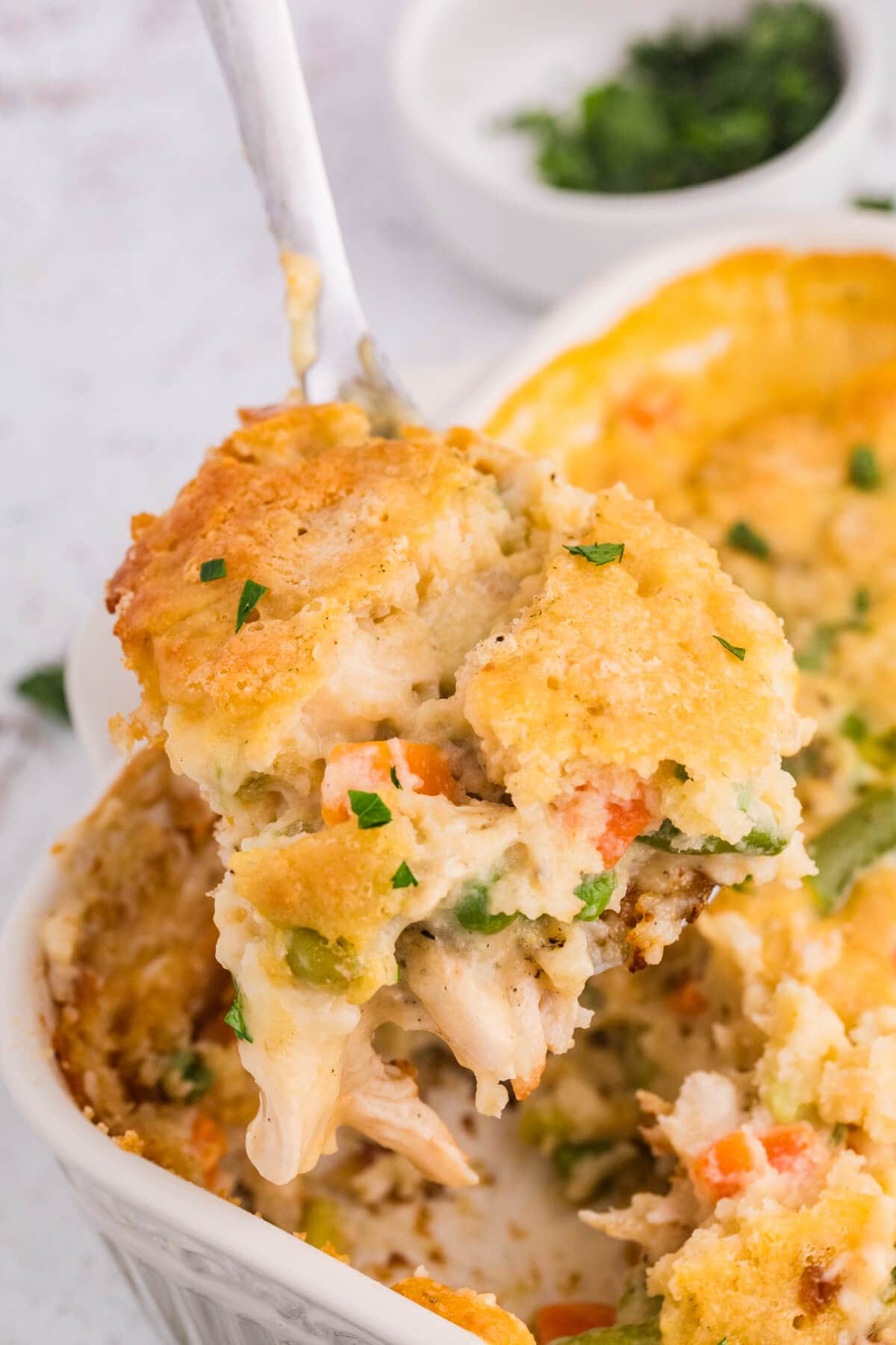 TikTok Chicken Cobbler being scooped from a baking dish with creamy chicken, mixed vegetables, and a golden Cheddar Bay biscuit topping.