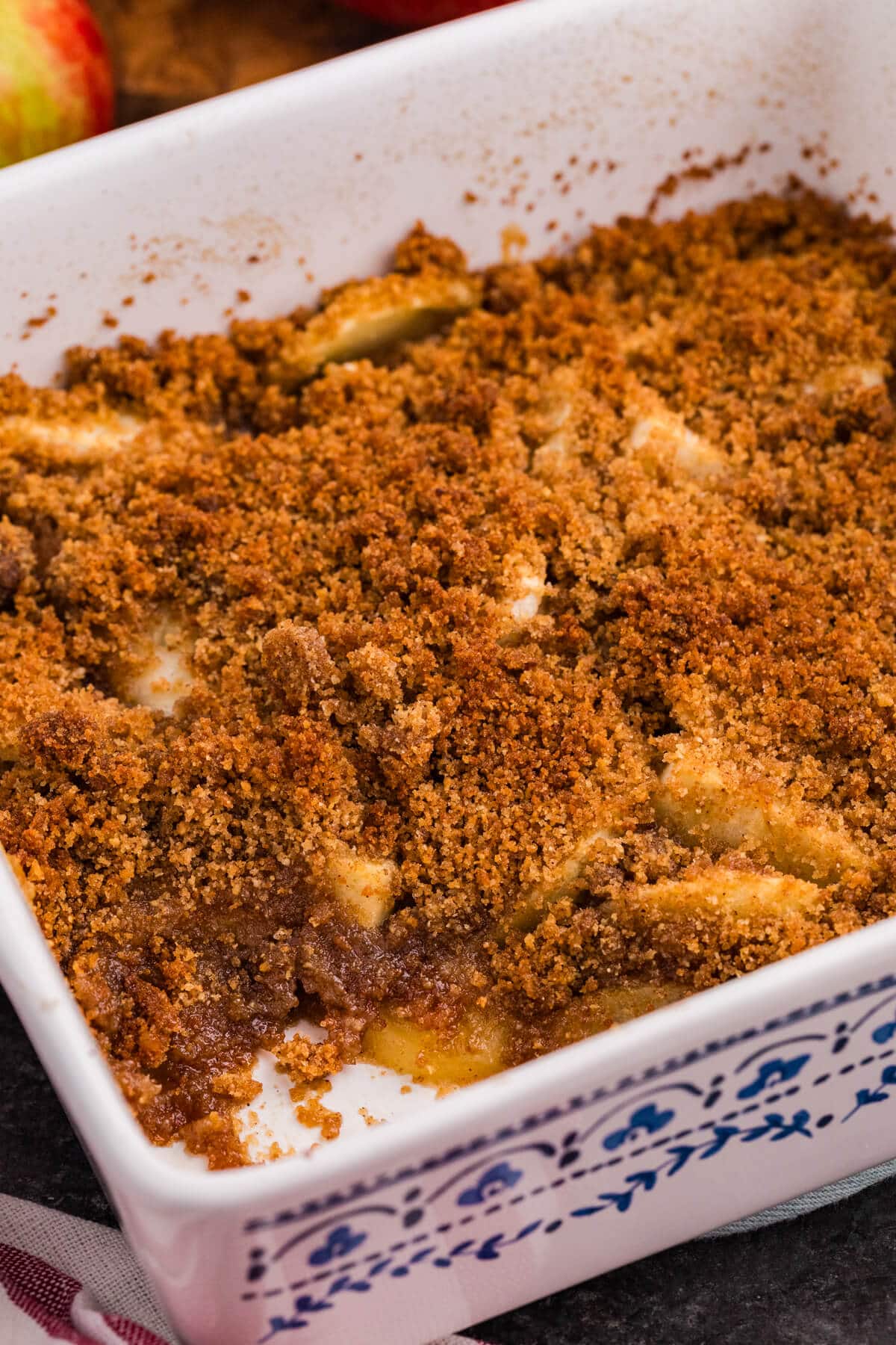 Baked apple brown betty in a white baking dish with a blue pattern, topped with golden brown breadcrumbs and a scoop missing from one corner.