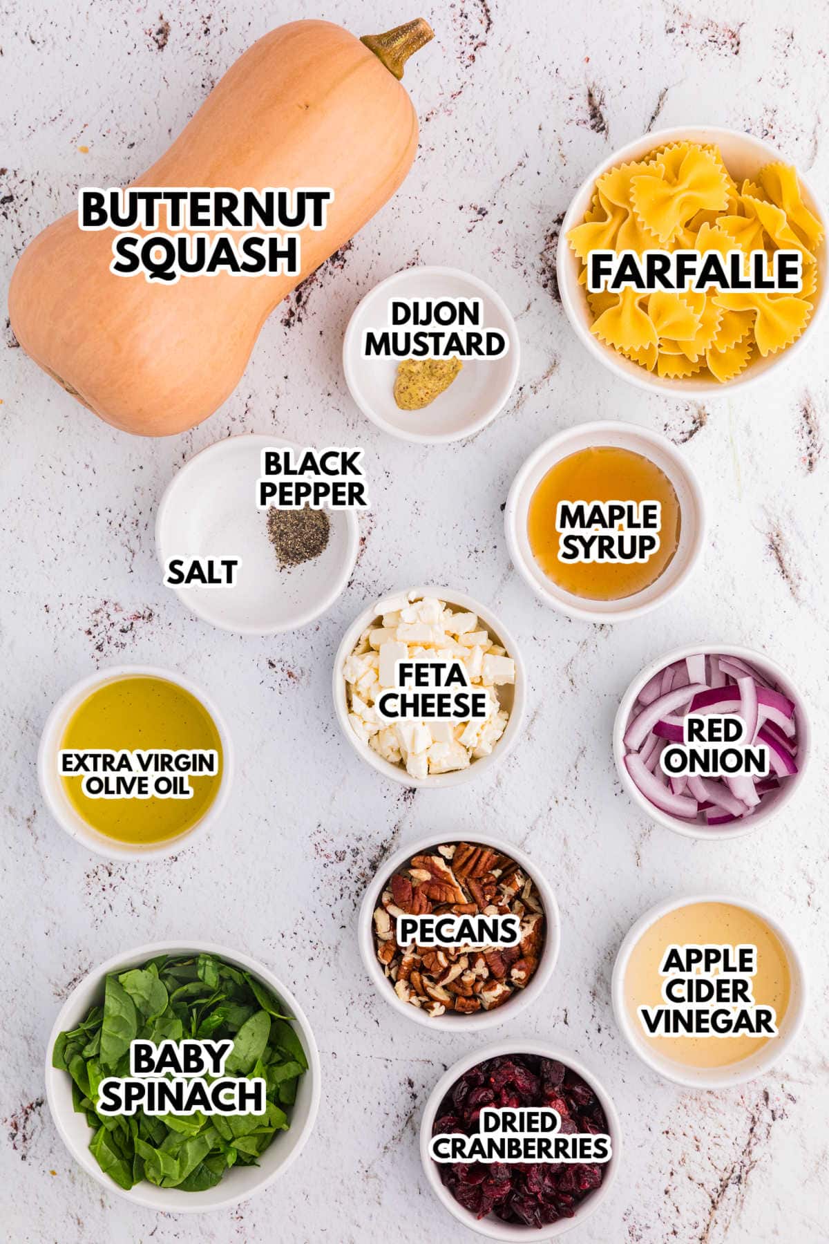 Overhead view of labeled fall pasta salad ingredients, including butternut squash, farfalle, pecans, cranberries, feta, and spinach, in small white bowls.