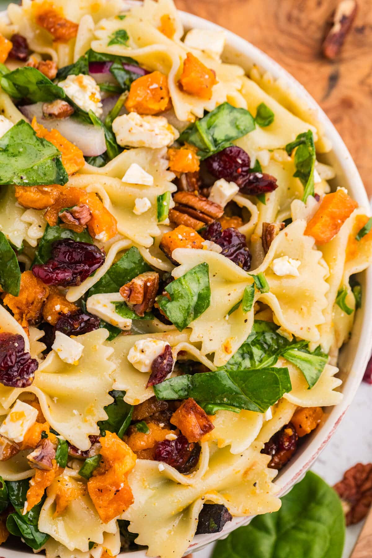 Up-close overhead view of fall pasta salad showing bow tie pasta coated in dressing with roasted butternut squash, spinach, cranberries, pecans, and feta.
