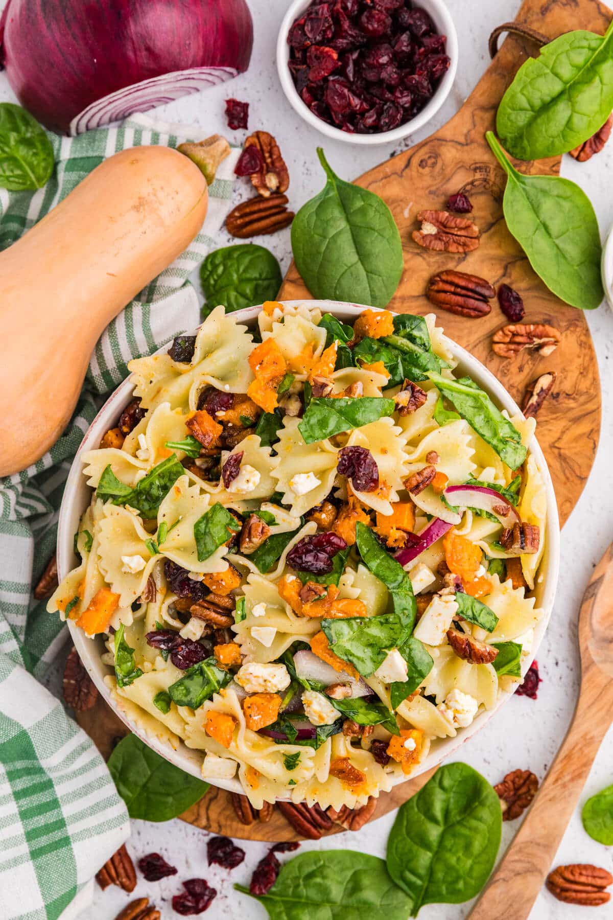 Overhead view of fall pasta salad with bow tie pasta, roasted butternut squash, spinach, cranberries, pecans, and feta in a white bowl.