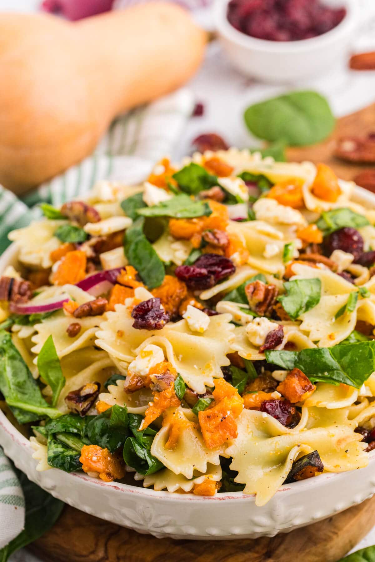 Close-up of fall pasta salad in a white bowl with bow tie pasta, roasted butternut squash, spinach, cranberries, pecans, and feta.