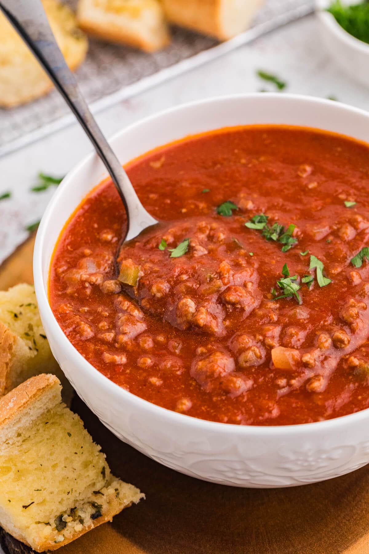 Spoon resting in a white bowl of thick, saucy Sloppy Joe Soup with ground beef and chopped parsley.