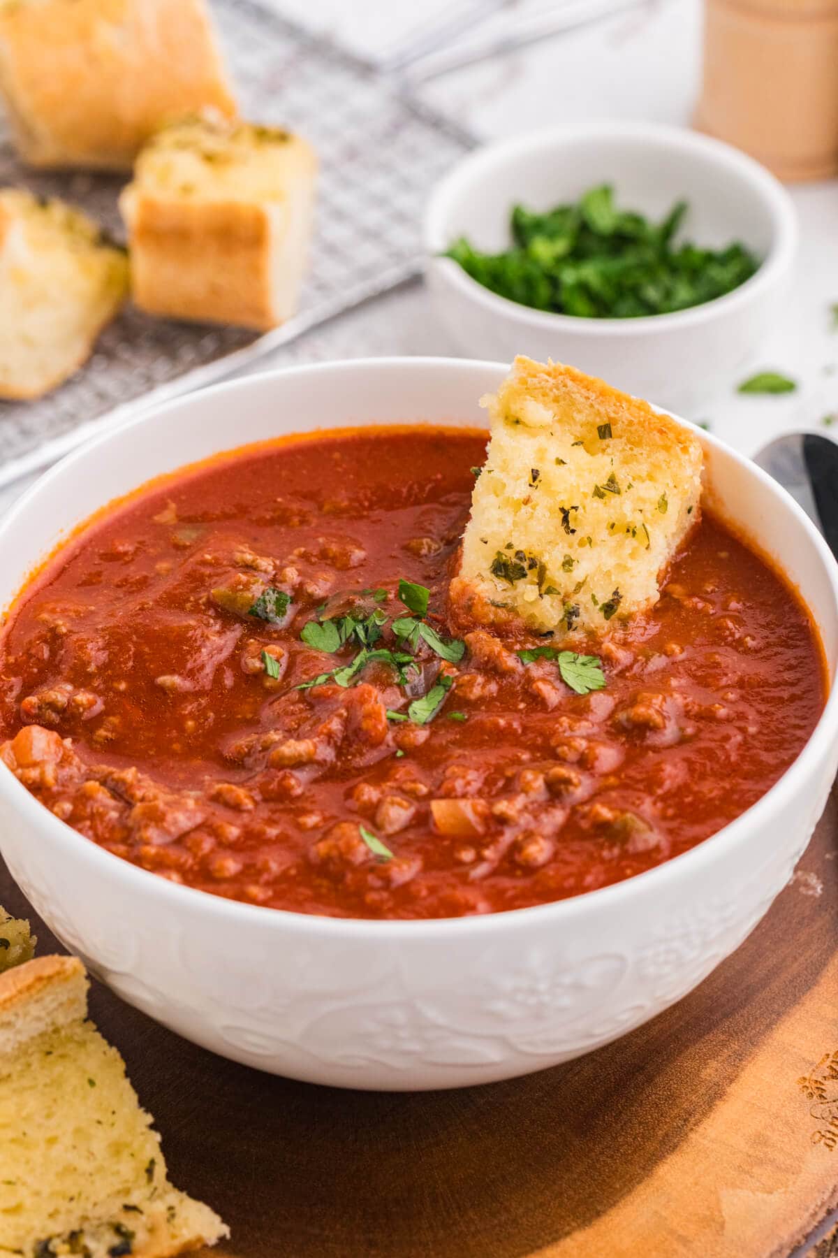 Bowl of thick Sloppy Joe Soup with ground beef, topped with parsley and a piece of garlic bread dipped in.