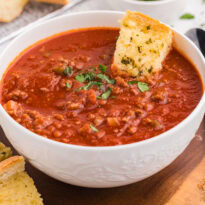 Bowl of Sloppy Joe Soup on a wooden board with slices of garlic bread and a spoon beside it.