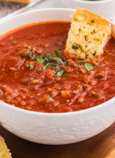 Bowl of Sloppy Joe Soup on a wooden board with slices of garlic bread and a spoon beside it.