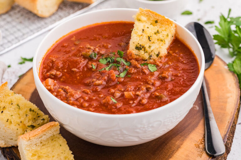 Bowl of Sloppy Joe Soup on a wooden board with slices of garlic bread and a spoon beside it.