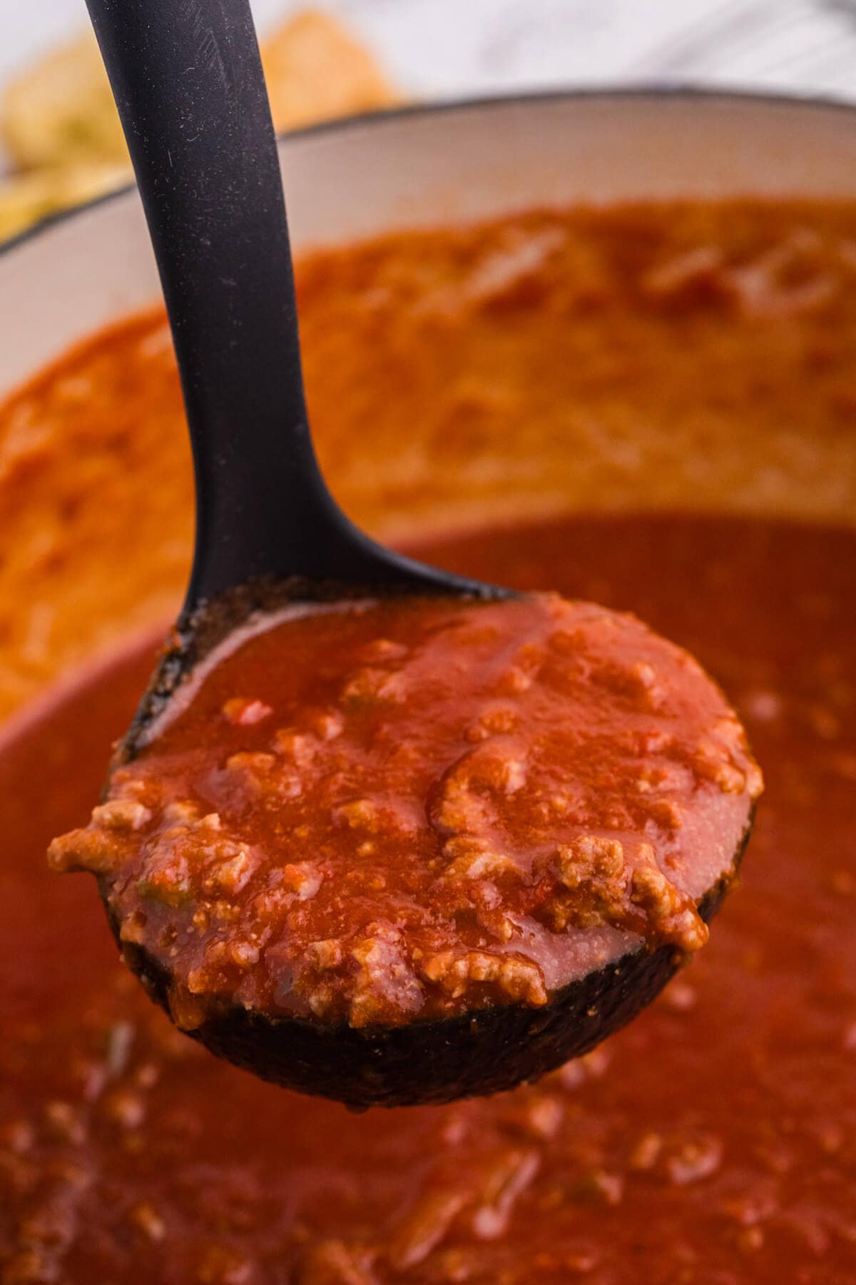 Ladle lifting thick tomato soup with ground beef out of a white pot.